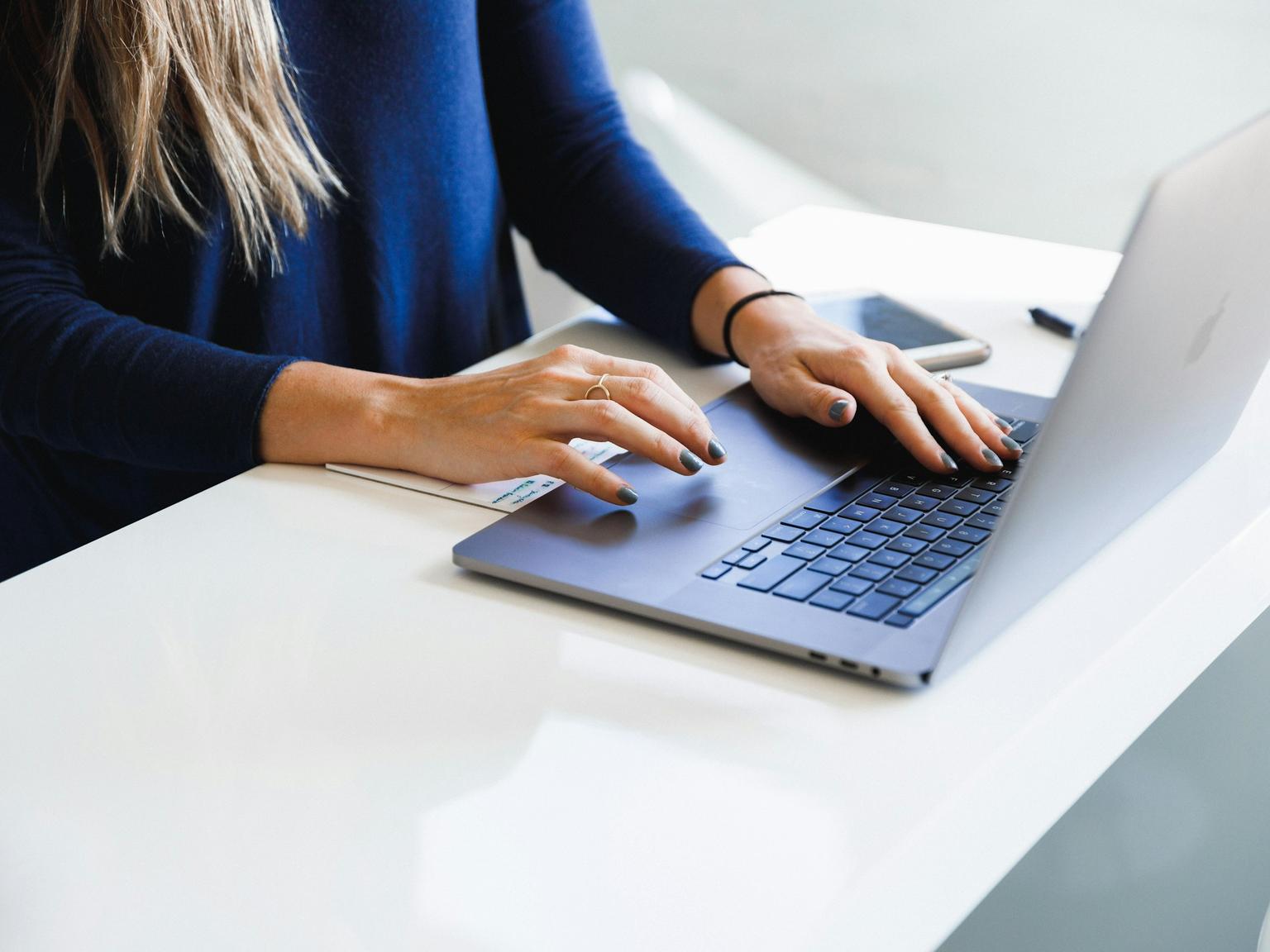 A person typing on a laptop at a bright white desk