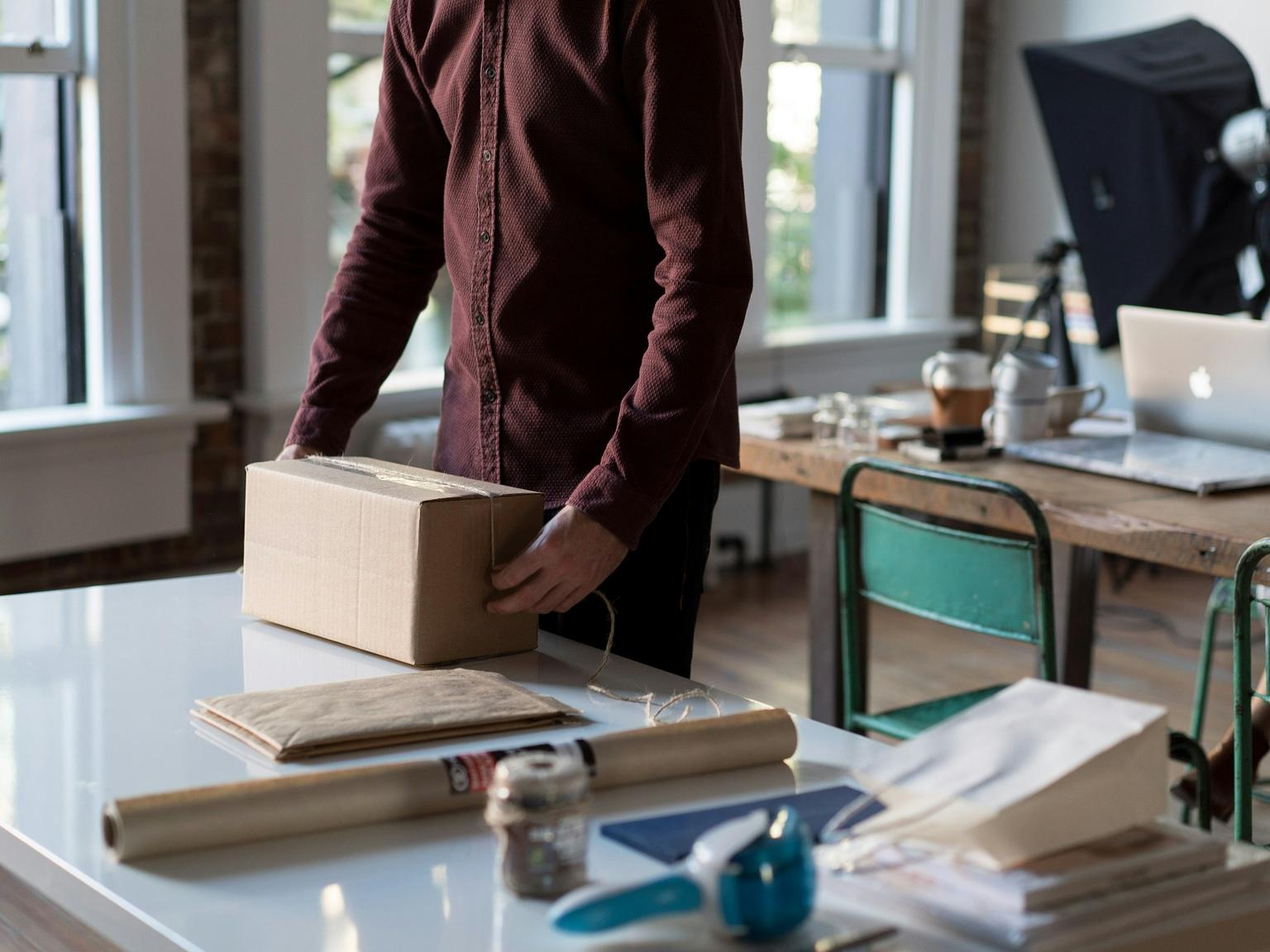 A person packing a cardboard box at a table in a bright workspace
