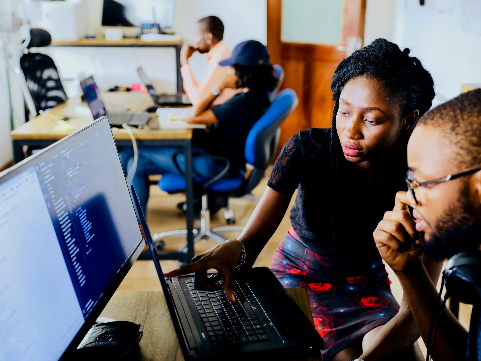 Two colleagues working through a problem together at a laptop and monitor