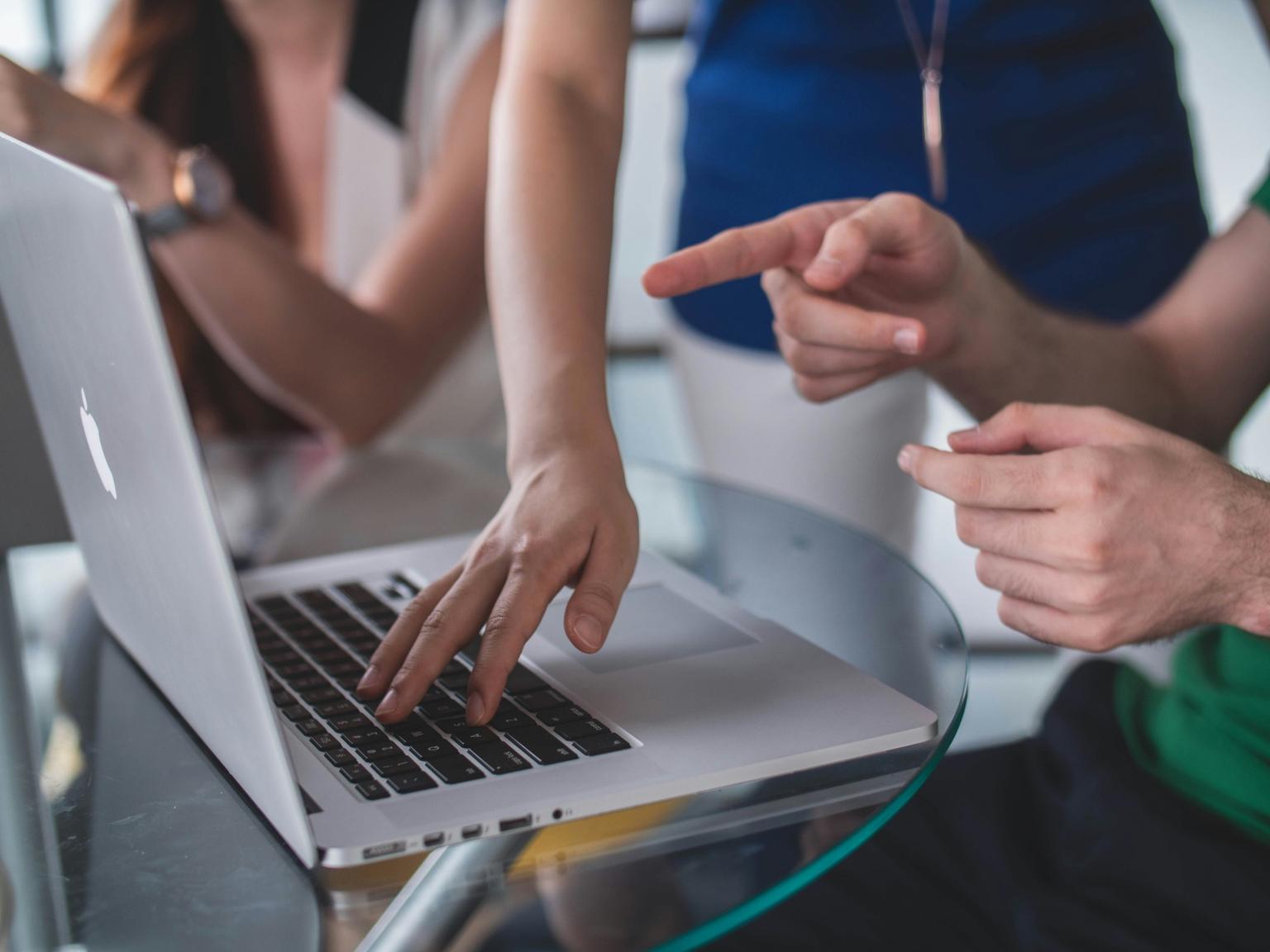Colleagues gathered around a laptop, one typing while another points at the screen